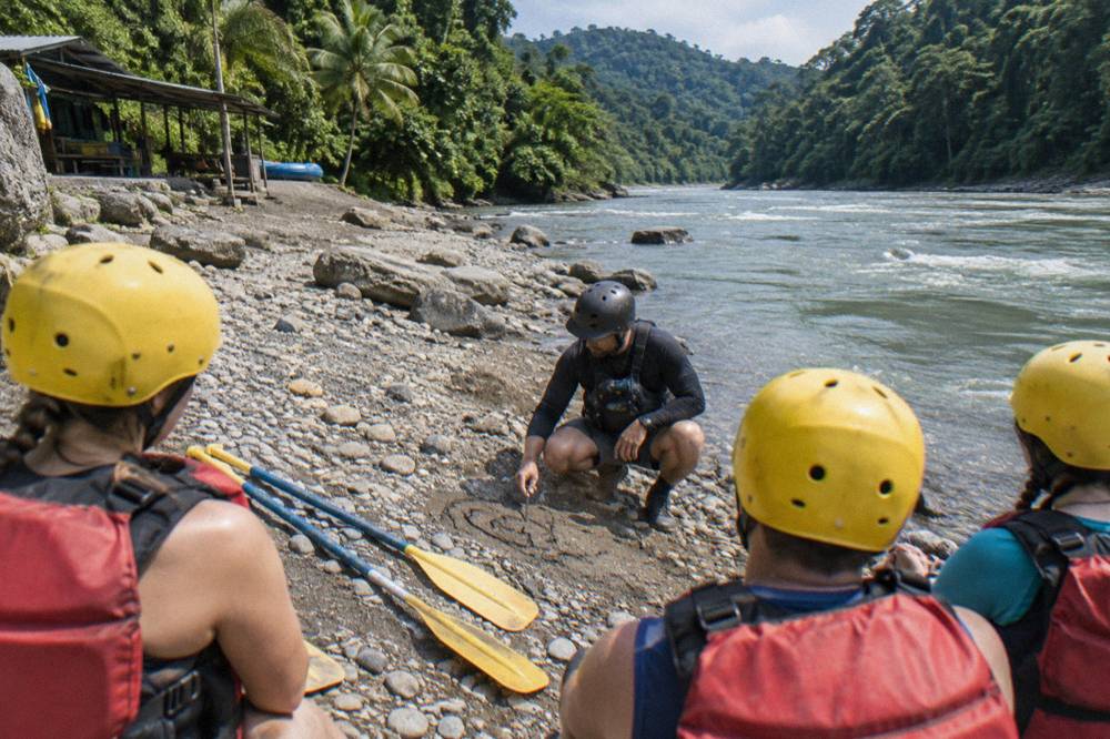 A guide giving a paddle briefing to a small group on a gravel riverbank
