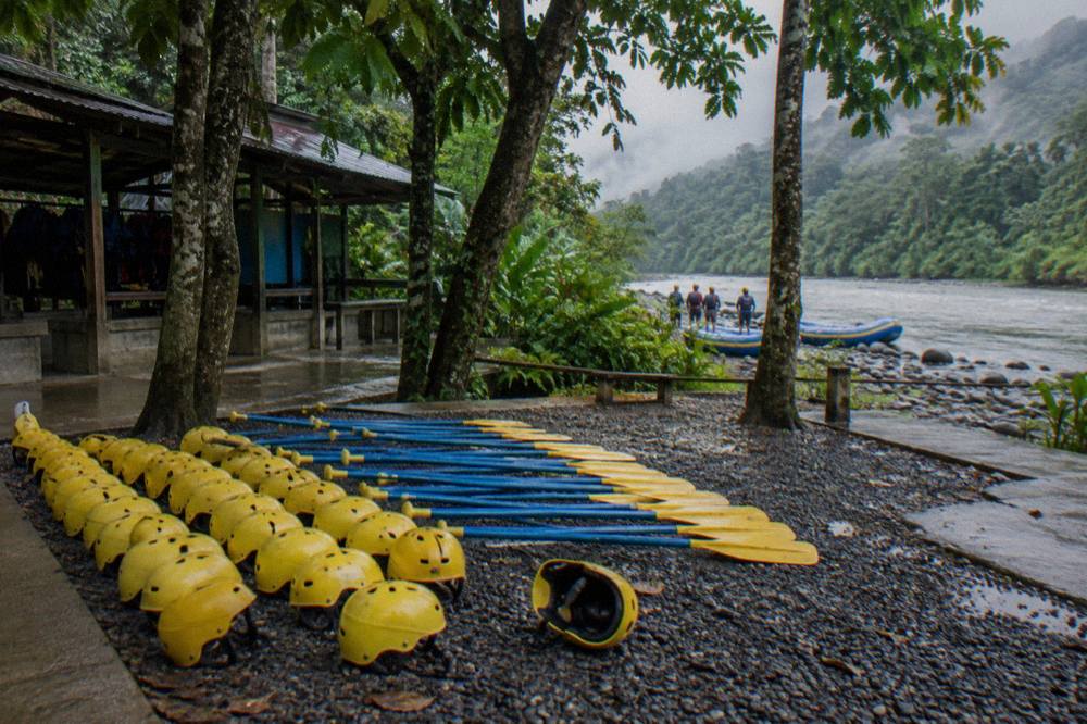 Rafting helmets and paddles laid out on a gravel riverbank before a trip briefing