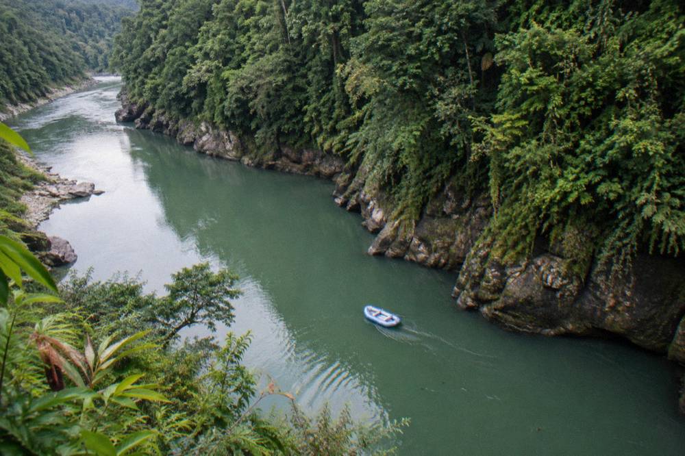 An inflated raft floating through calm green water between steep rainforest canyon walls