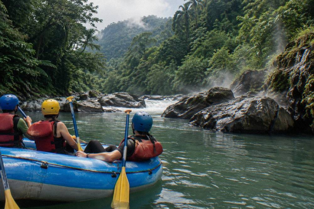 A raft resting in a calm green pool between rapids with paddlers leaning on their paddles