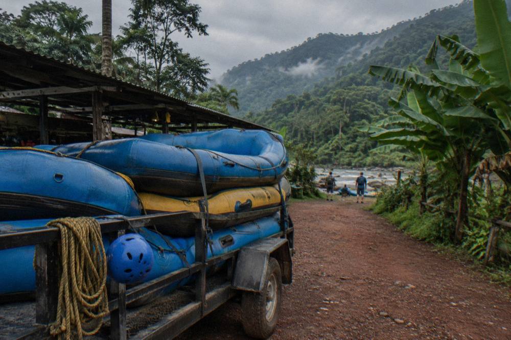 A loaded raft trailer parked beside a dirt road at the edge of a rainforest
