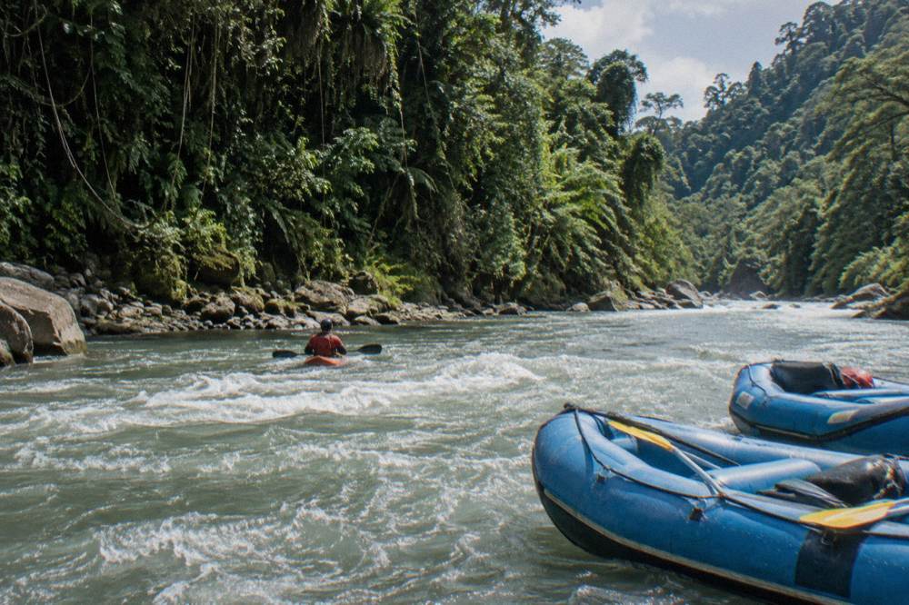 A safety kayaker holding position in the current beside rafts on a jungle river