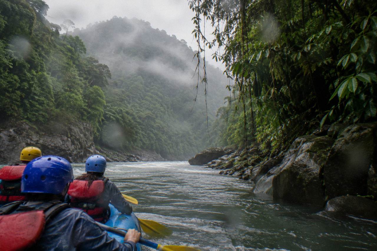 A raft with paddlers in helmets and life jackets moving through a green jungle gorge on the Pacuare River