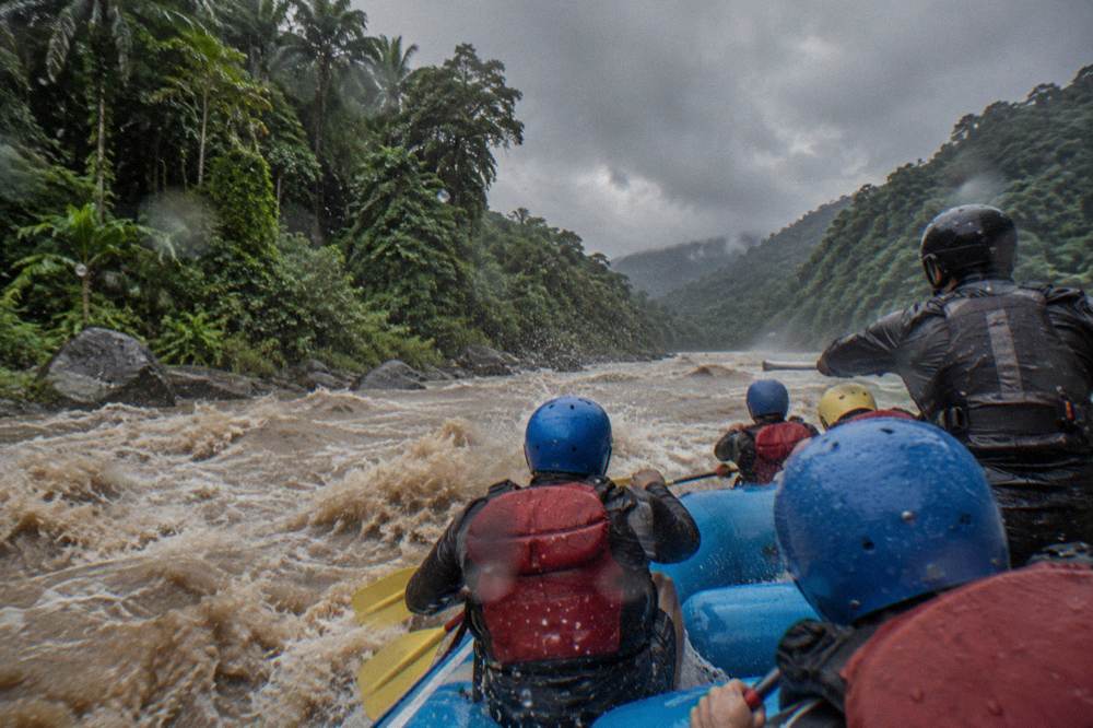 A raft crew paddling through a wave train with a guide calling commands at the stern