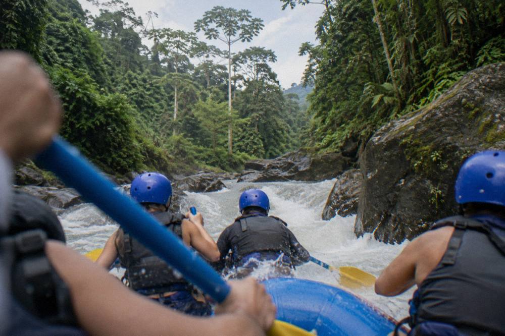 A raft passing through a narrow rocky rapid with dense rainforest on both banks
