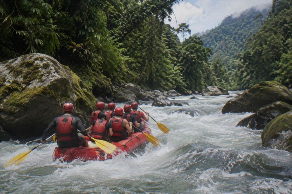 Rafters in helmets and life jackets paddling in sync through a wave train