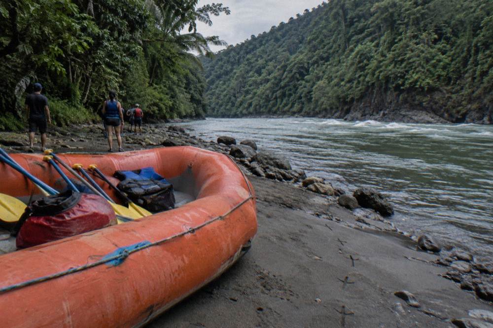 A raft resting on a gravel bar beside a jungle river at sunset