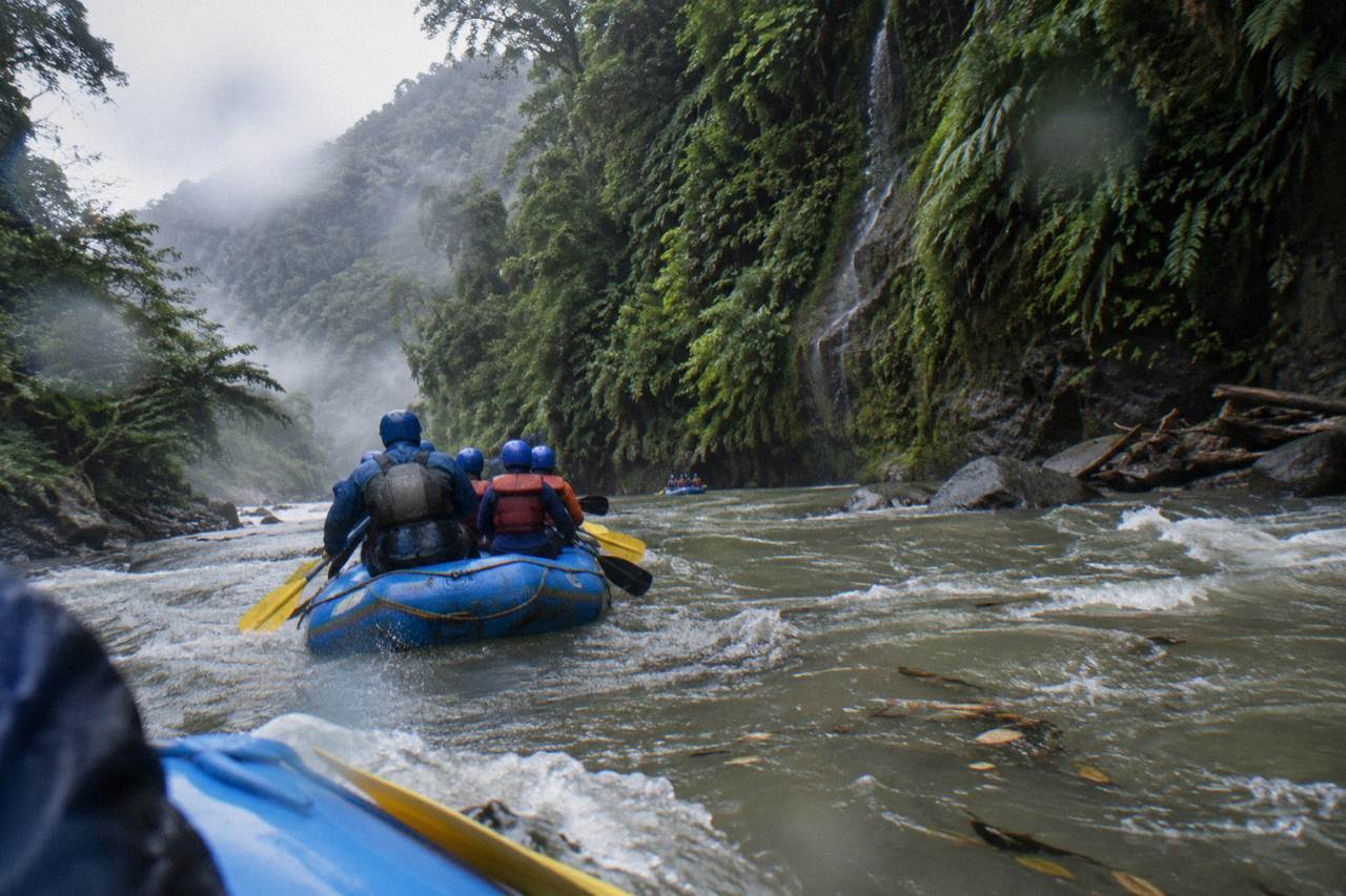 A raft cutting through a green jungle gorge with mist on the canyon walls