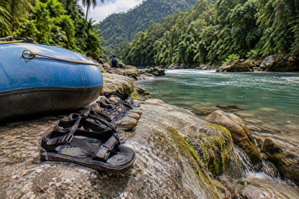 Close view of strapped river sandals and worn sneakers drying on rocks beside a raft