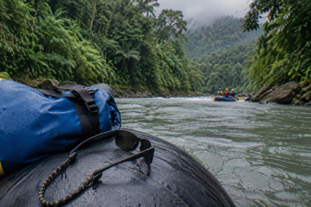 Sunglasses with a retainer strap and a small dry bag resting on a raft tube before departure