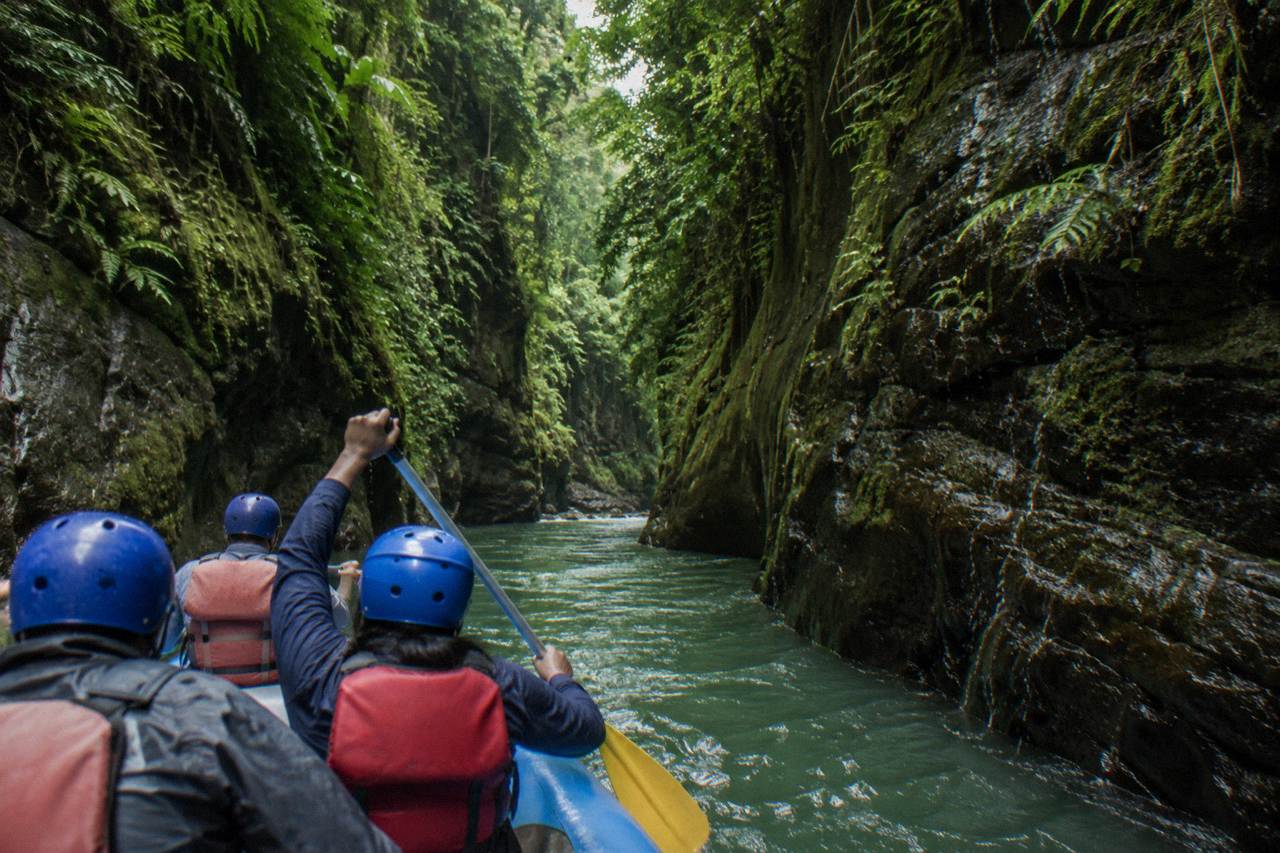A raft cutting through a narrow jungle gorge with green canyon walls rising on both sides