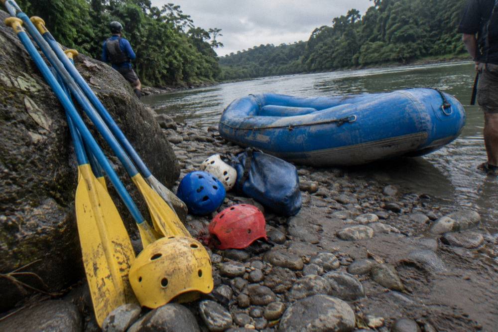 Helmets and paddles laid out on a riverbank ready for a rafting trip