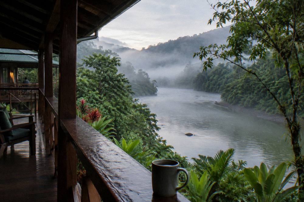 A calm stretch of river in early morning light with mist over the water and jungle hills behind