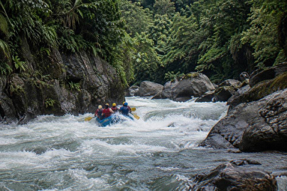 A raft of paddlers in helmets and life vests entering a wave train in a narrow green canyon