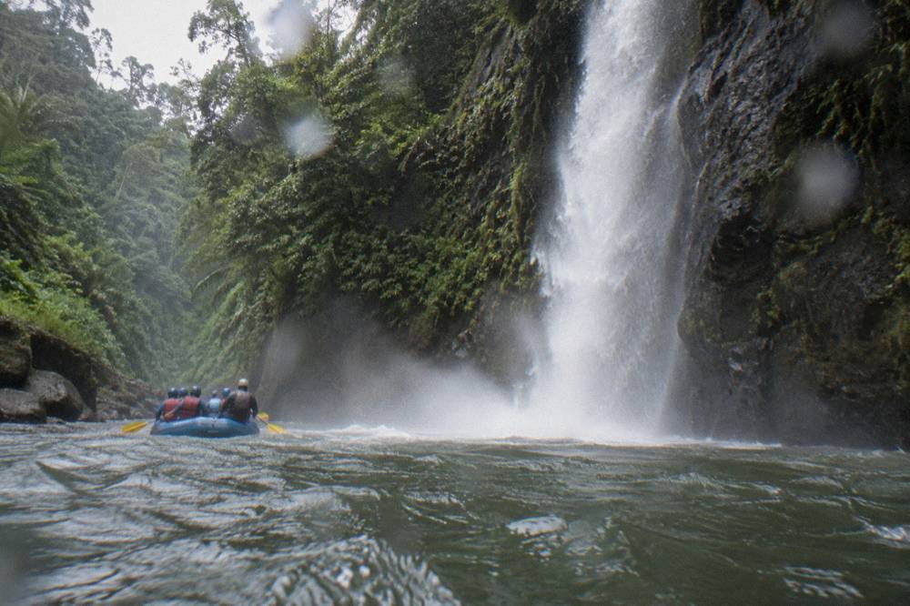 A narrow canyon rapid with a tall waterfall pouring off the rock wall beside the river