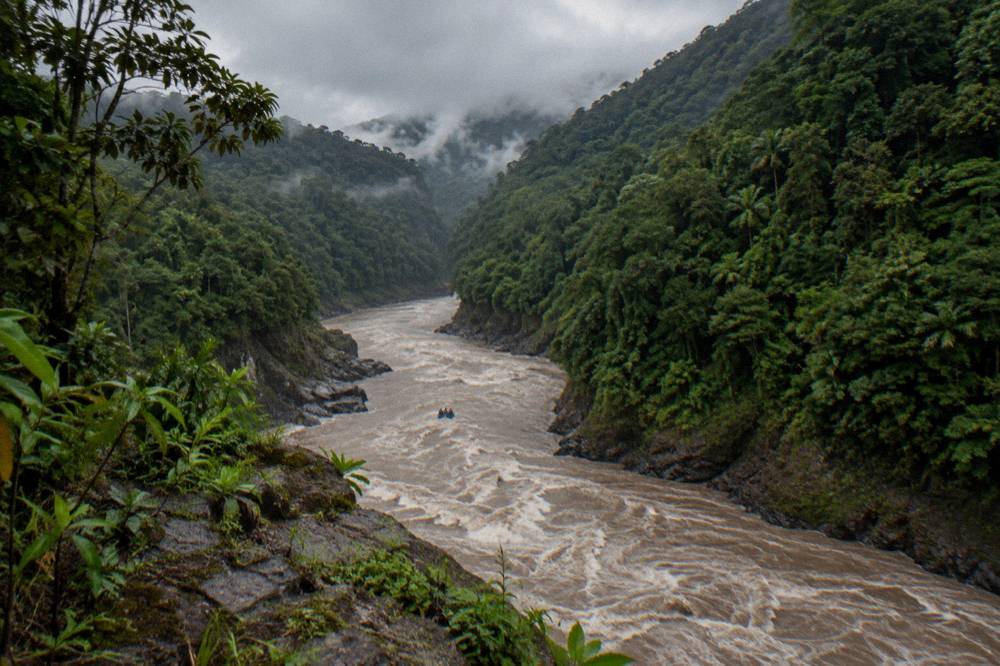 A wide jungle river with a raft small in the distance between steep forested banks