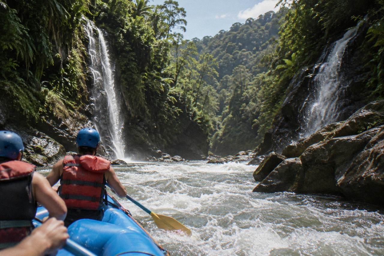A raft pushing through a steep green canyon rapid with waterfalls on the rock walls