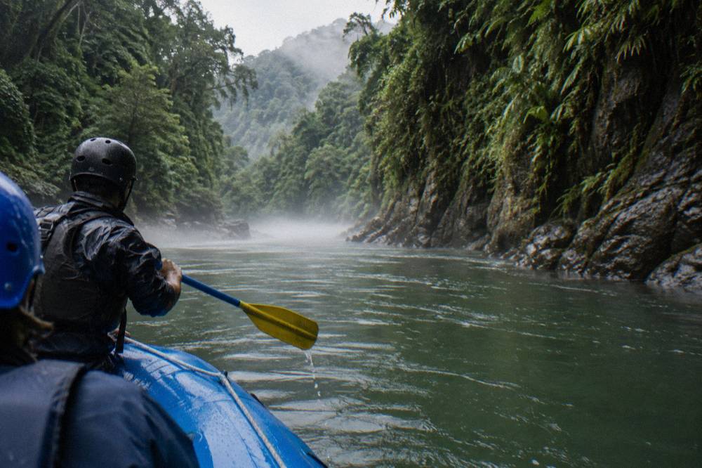 A raft passing through a narrow jungle canyon with mist on the water
