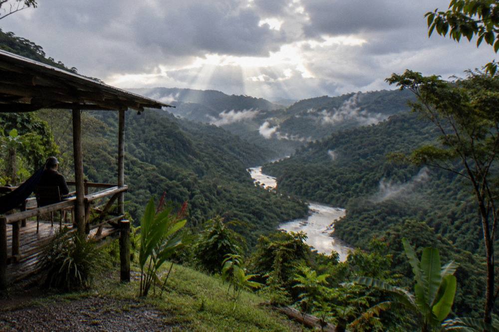 Sunlight breaking through rain clouds over a wide green valley with a river below