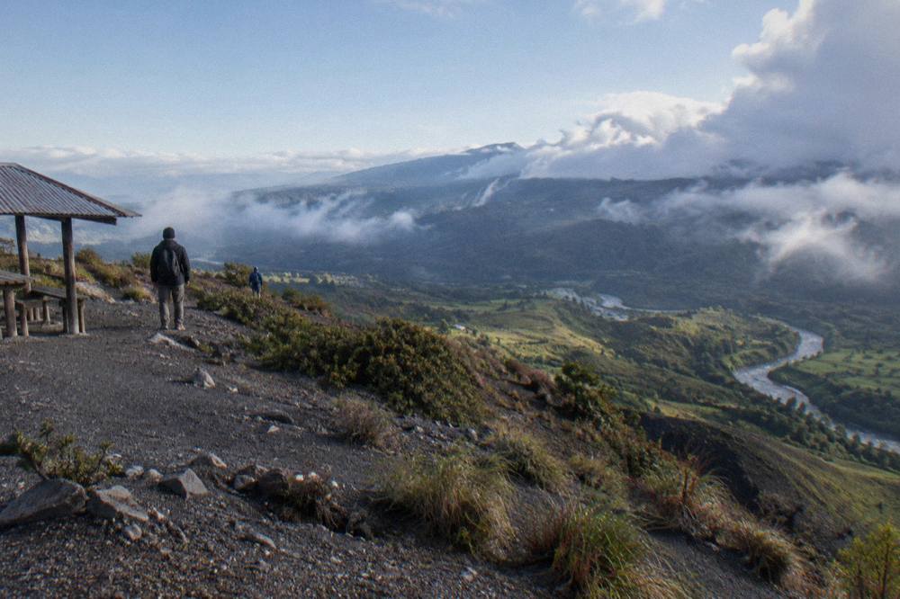 A green valley with a volcano rising above farmland and morning mist