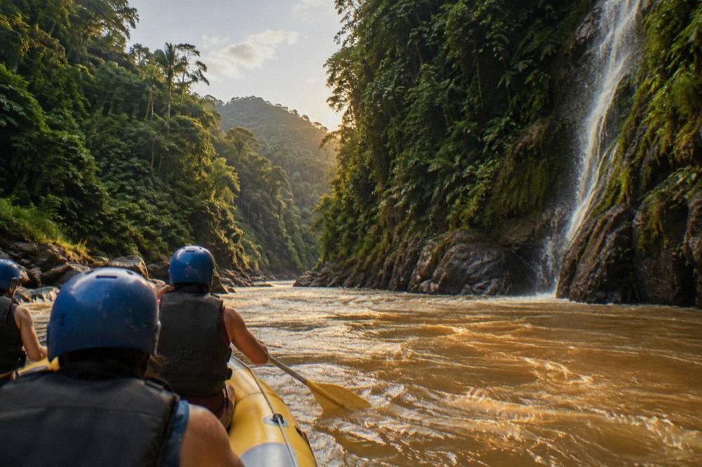 A raft passing between steep rainforest canyon walls with a waterfall on one side