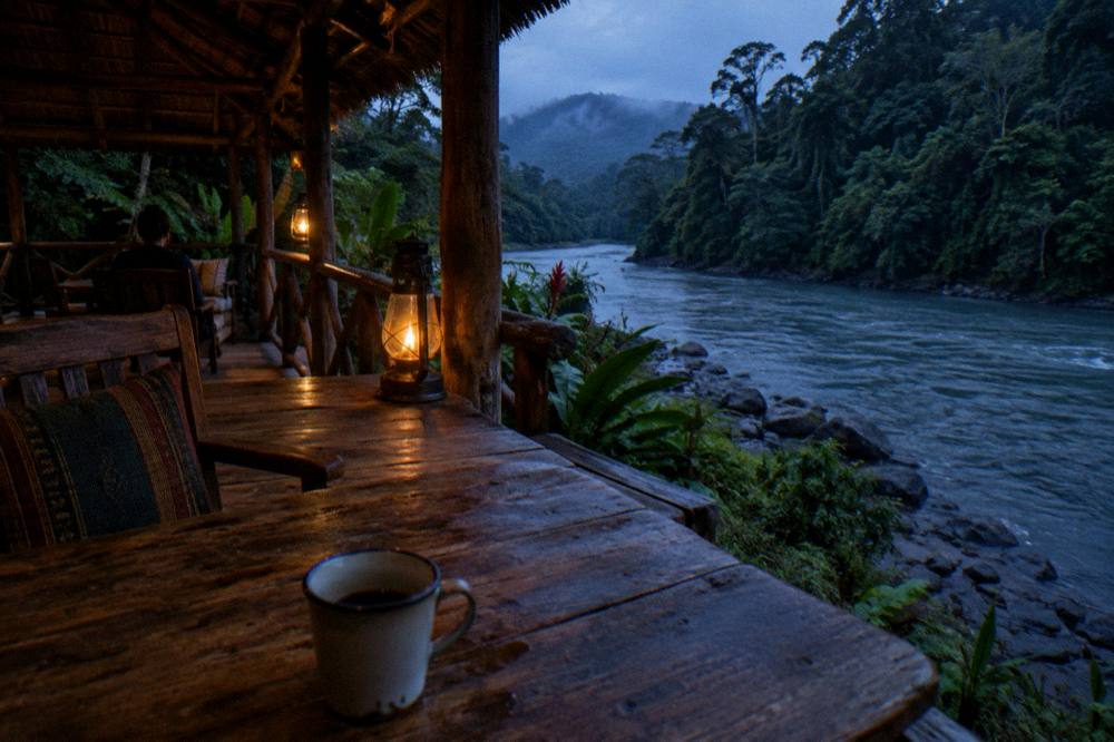 A wooden riverside ecolodge porch overlooking a jungle river at dusk