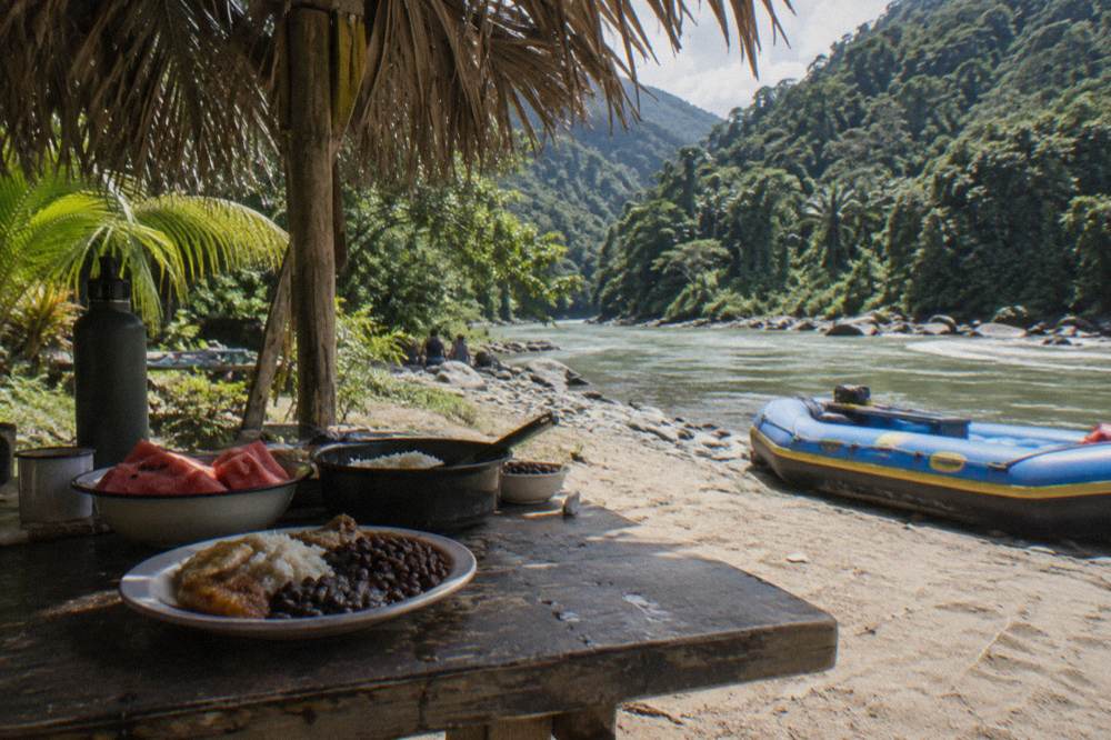 Riverside lunch spread served on a table beside the Pacuare River after a rafting run