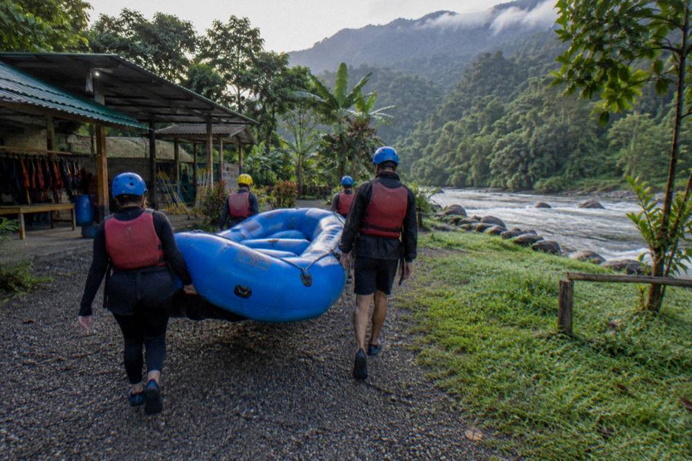 Paddlers in helmets and life vests carrying a raft toward the river bank at the put-in