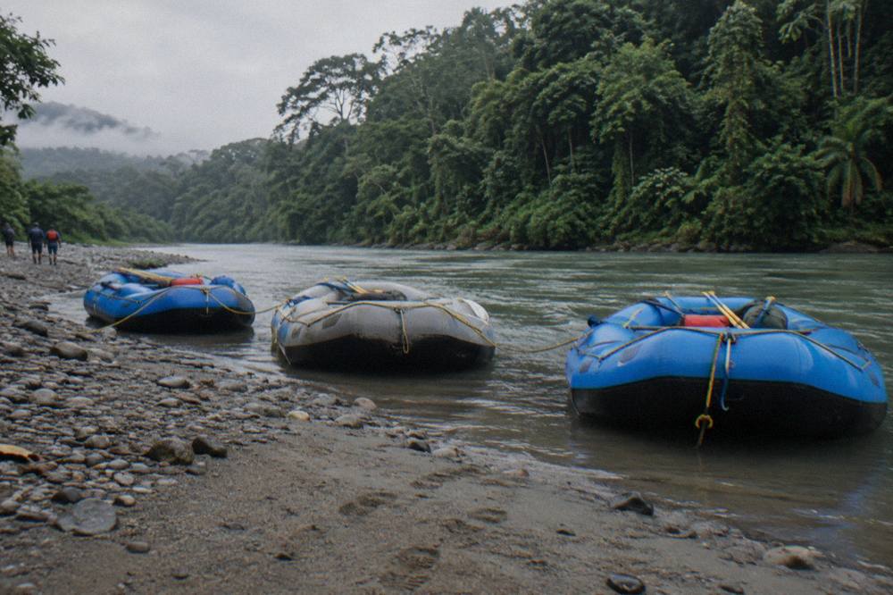 A line of rafts tied at a gravel bar on the Pacuare River with dense jungle on the far bank