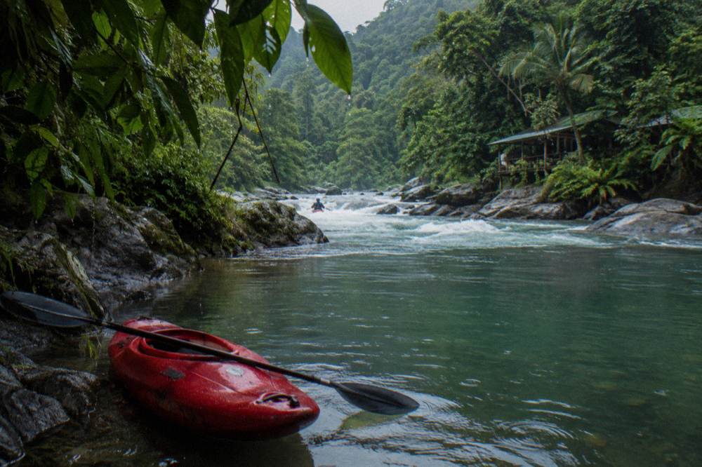 A safety kayak waiting in an eddy beside a calm green pool between rapids