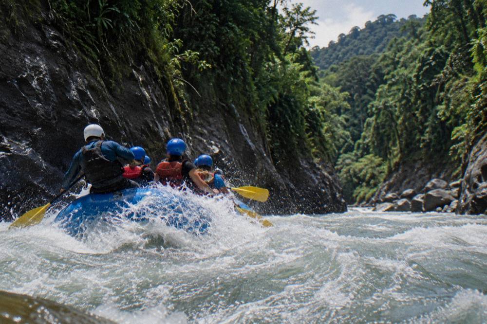 A raft carrying paddlers through a foamy green wave train between canyon walls
