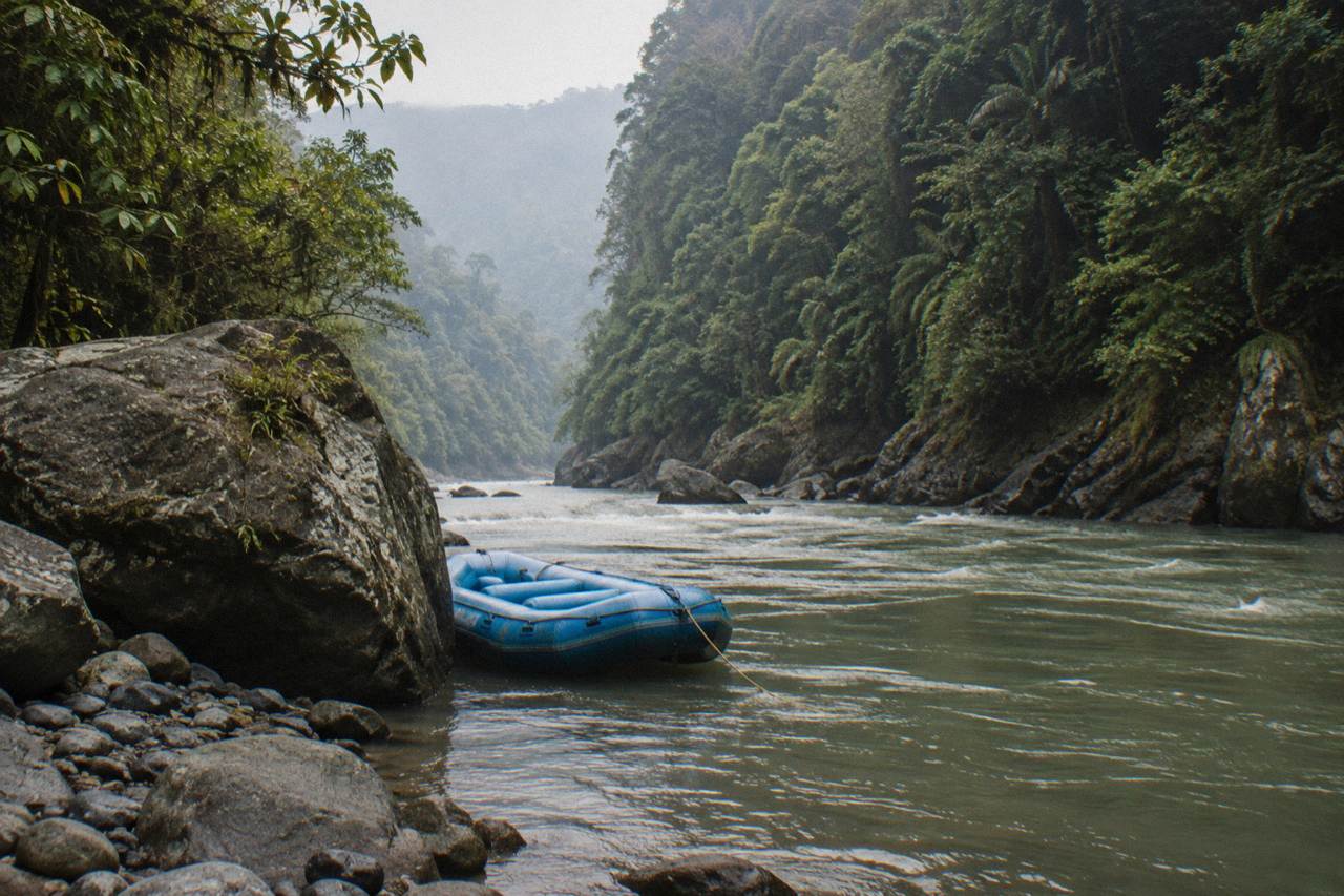 A raft resting on a boulder beside the green Pacuare River gorge with rainforest walls rising on both sides