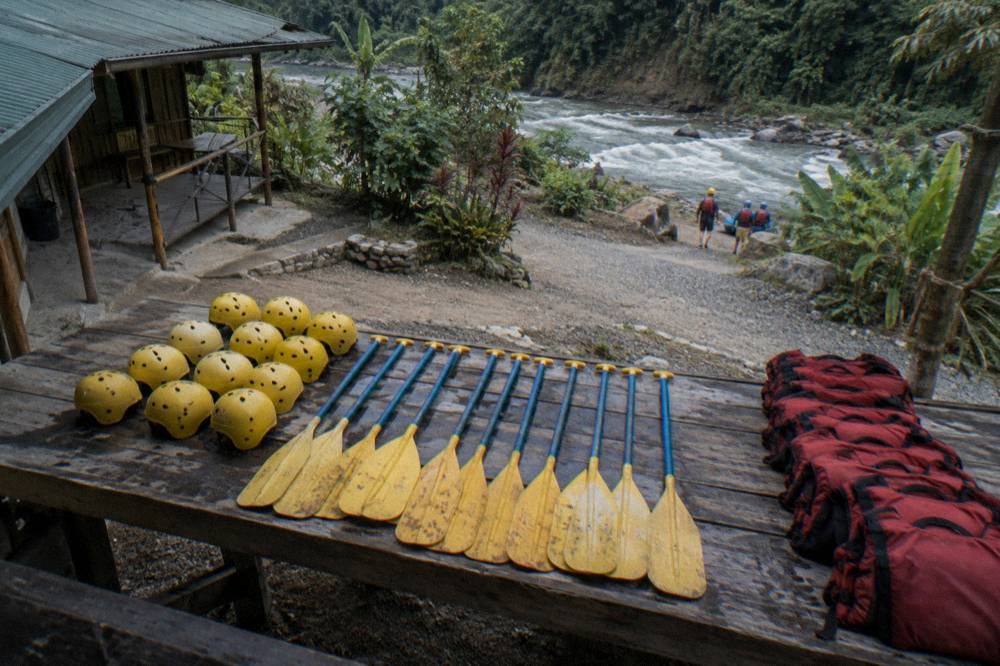 Neatly arranged rafting gear including helmets, paddles and life jackets on a riverbank bench