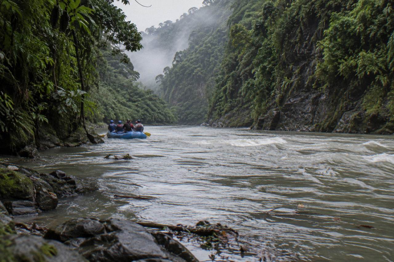 A raft cutting through a green jungle gorge on the Pacuare River with mist on the canyon walls