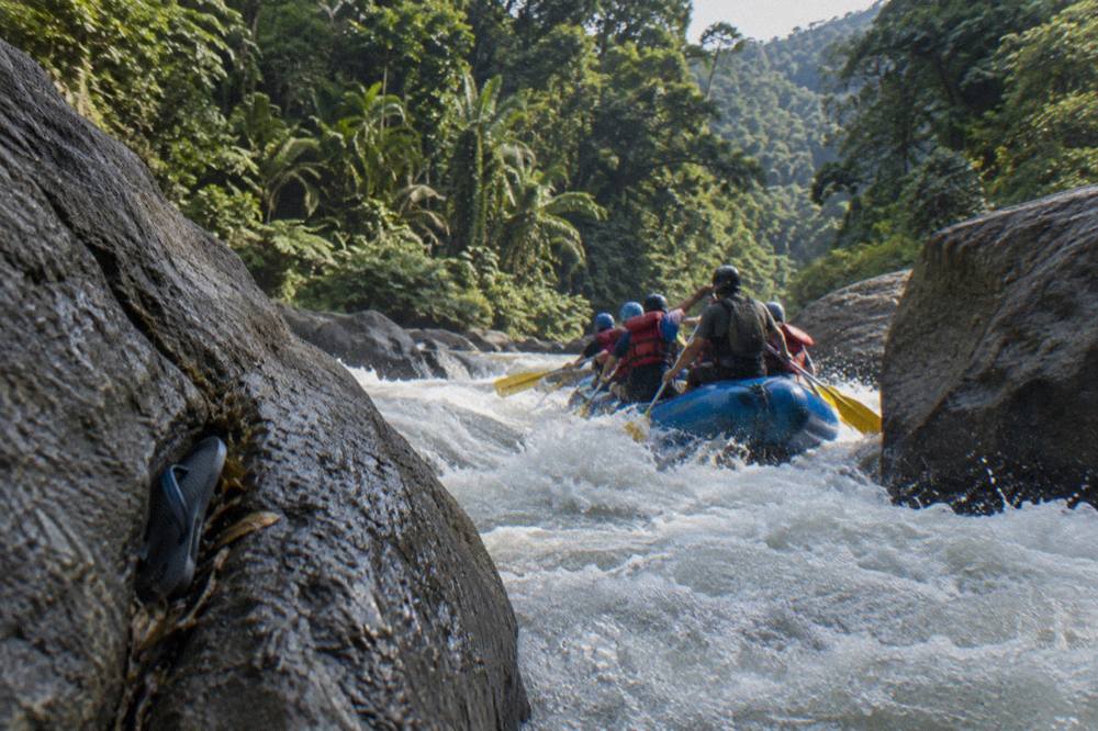 A raft crew paddling through a foamy rapid between boulders