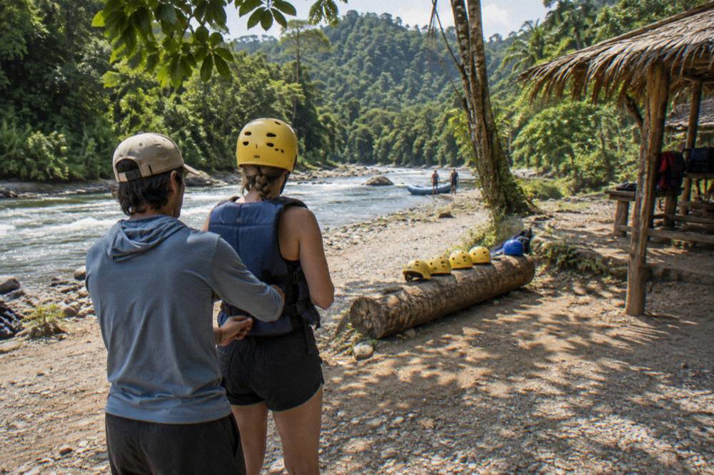 Guides fitting helmets and life jackets on raft crew members at a riverbank