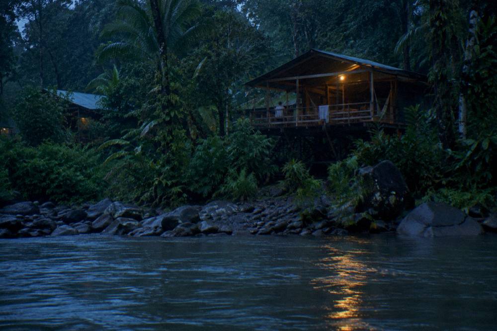 Riverside jungle lodge cabin overlooking a rainforest river at dusk