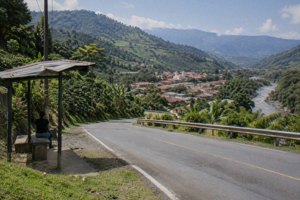 A paved mountain road winding through green hills toward a valley town