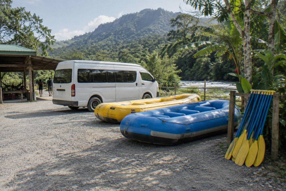 A shuttle van parked beside rafts and paddles at a river staging area