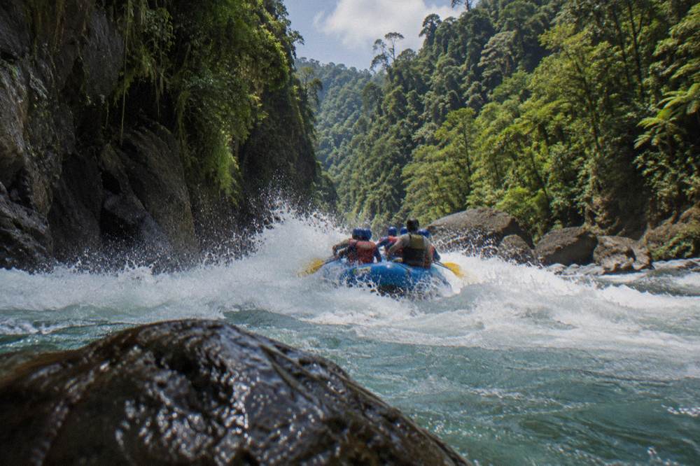 A paddle raft crashing through a whitewater wave between steep canyon walls