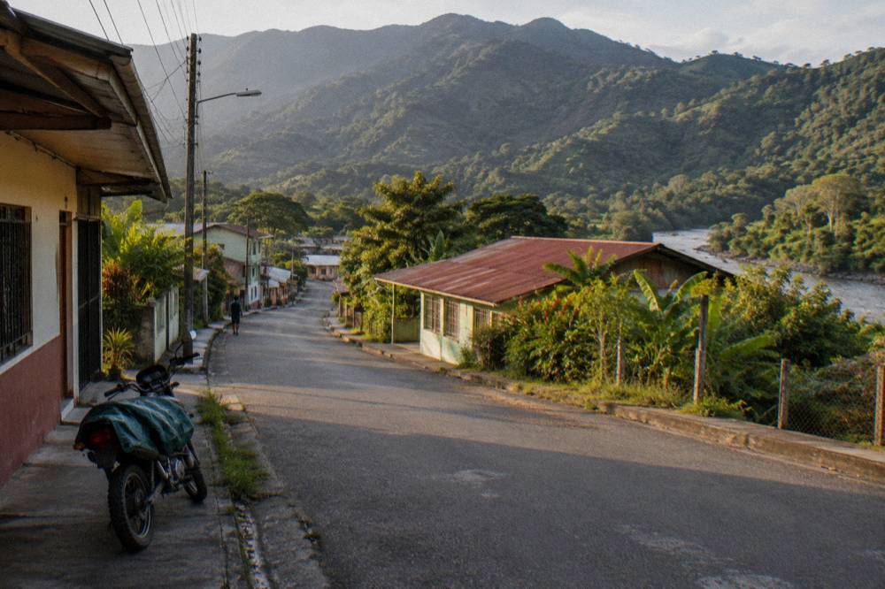 A quiet hillside town street with green mountains behind low buildings