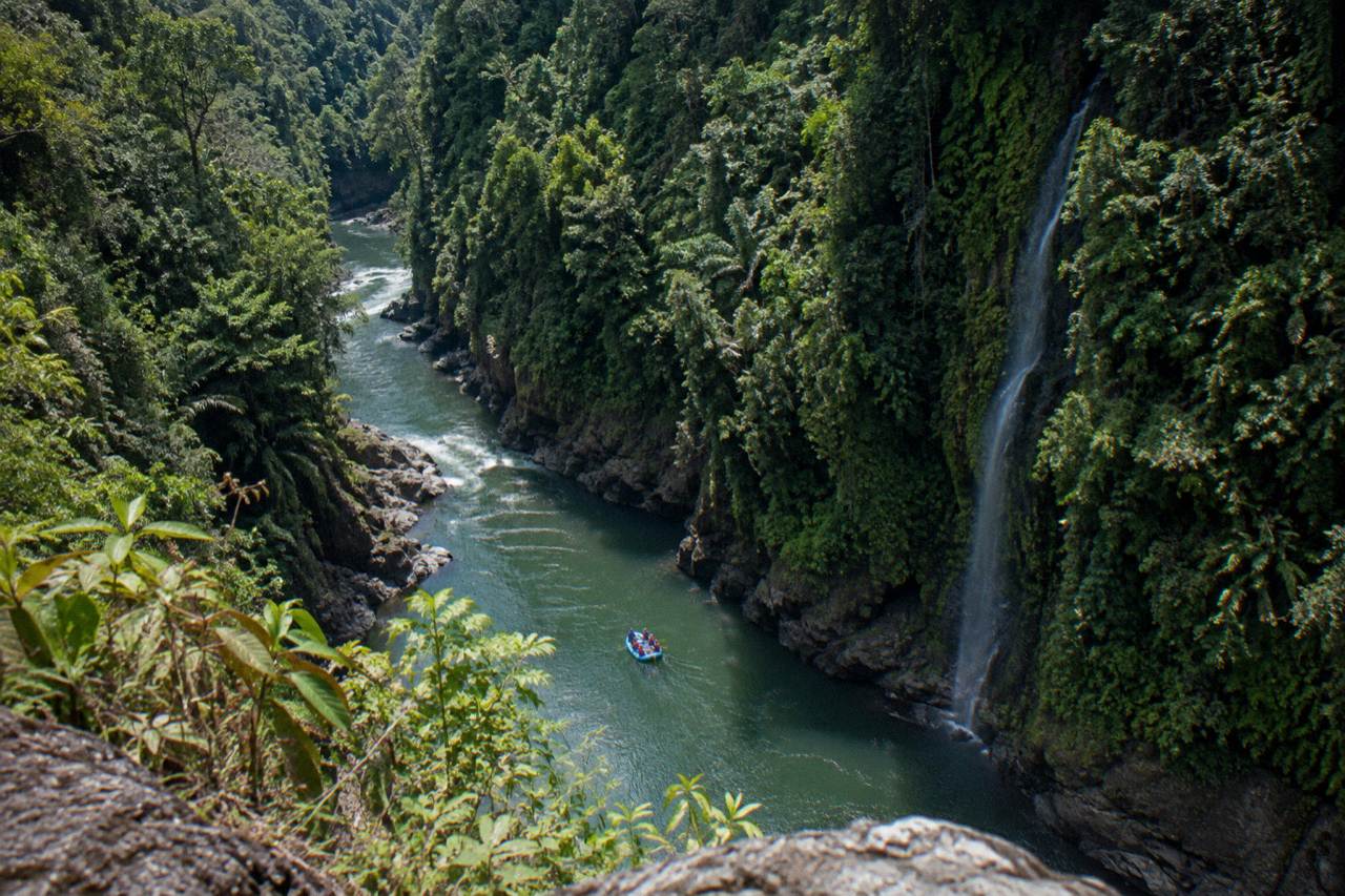 A raft drifting through a narrow jungle gorge with tall green canyon walls
