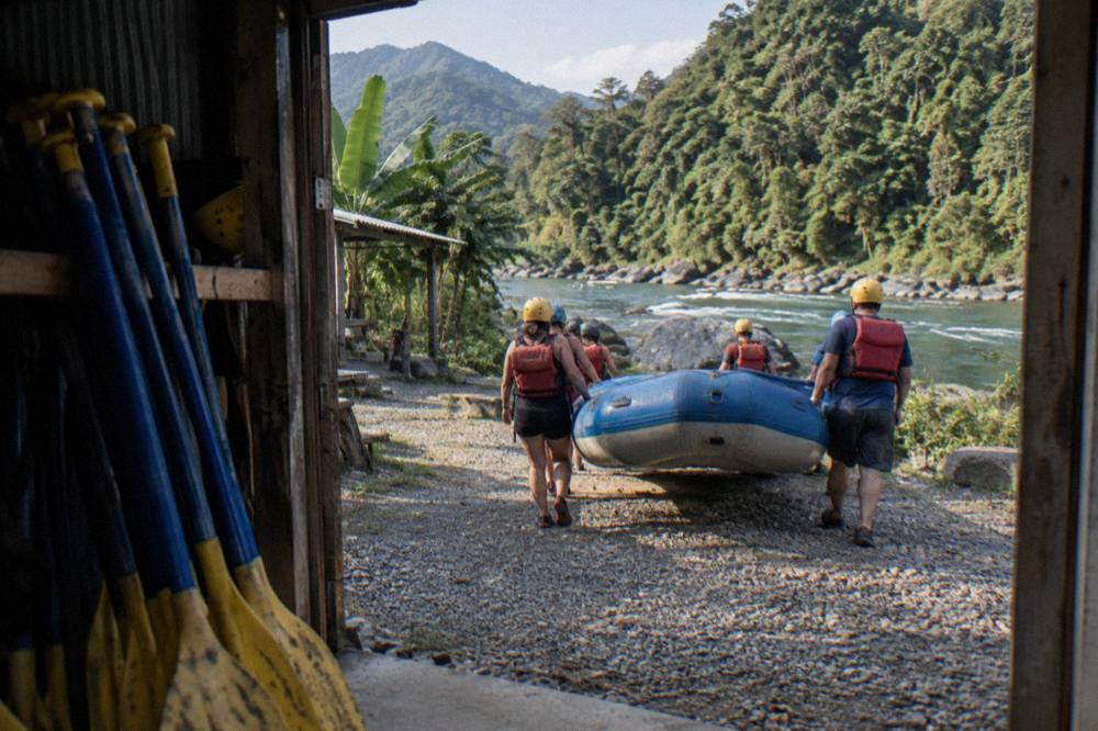 Rafting guests in helmets and life vests carrying a raft toward the riverbank