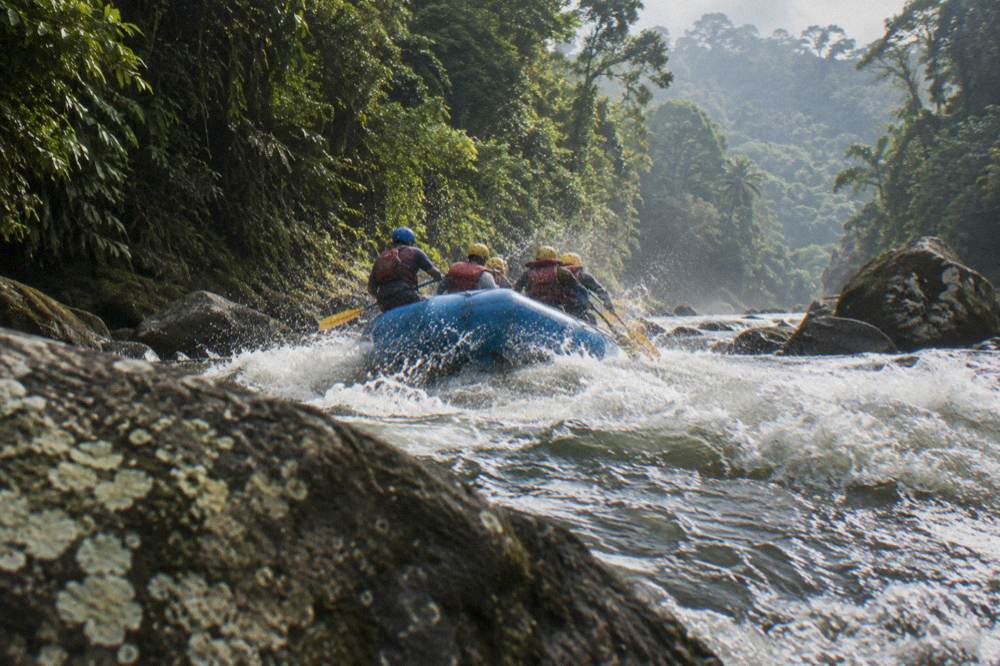 Paddle raft cresting a wave in a rocky jungle rapids section