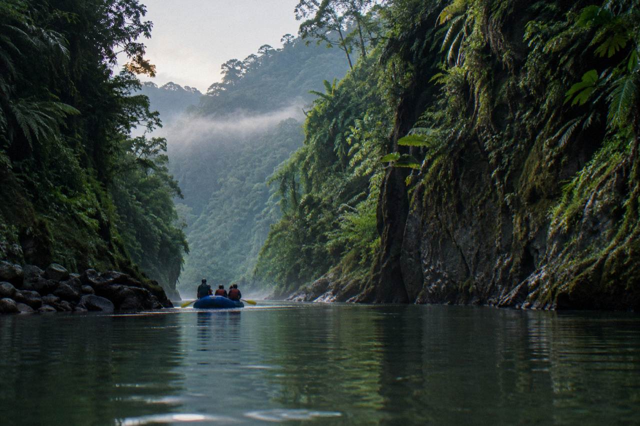 Raft floating through a narrow jungle gorge with tall green canyon walls