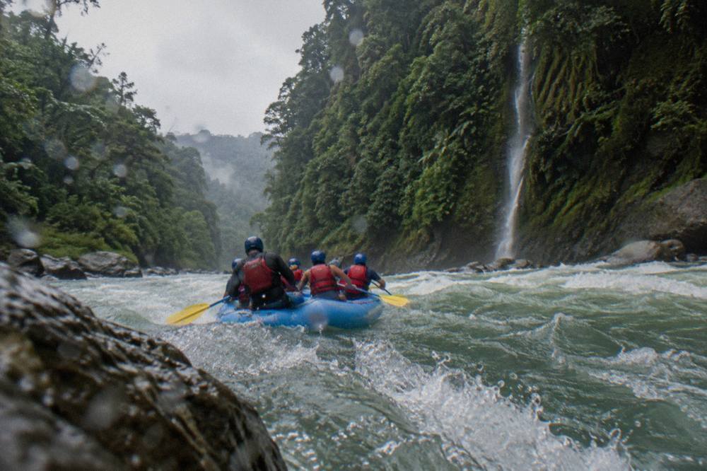 Rafting paddlers in helmets and life vests on turbulent green whitewater between forested canyon walls