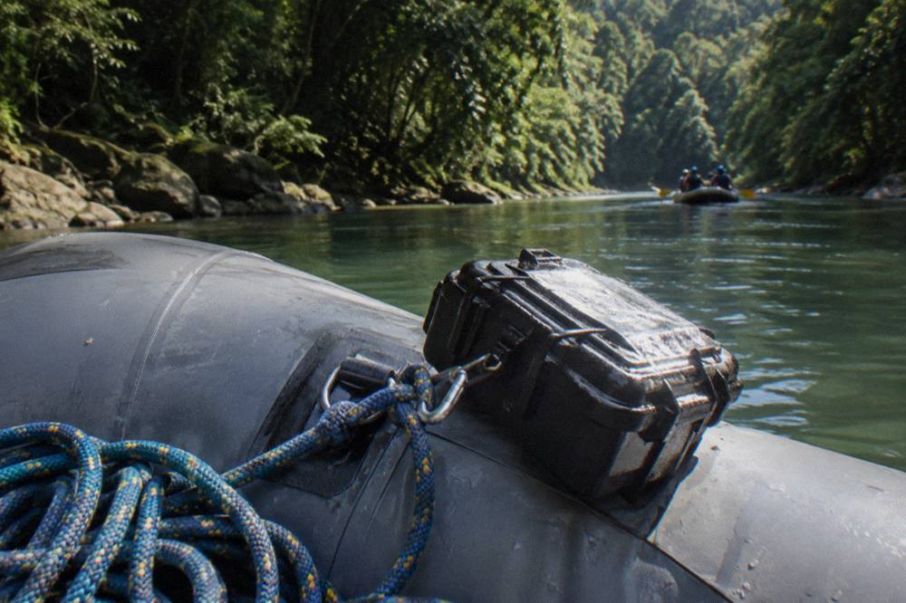 A waterproof camera case clipped inside an inflatable raft on a jungle river