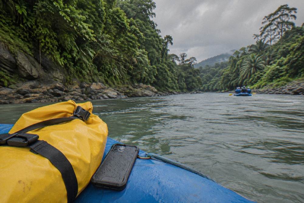 A roll-top dry bag and a hard waterproof phone case resting on a raft tube