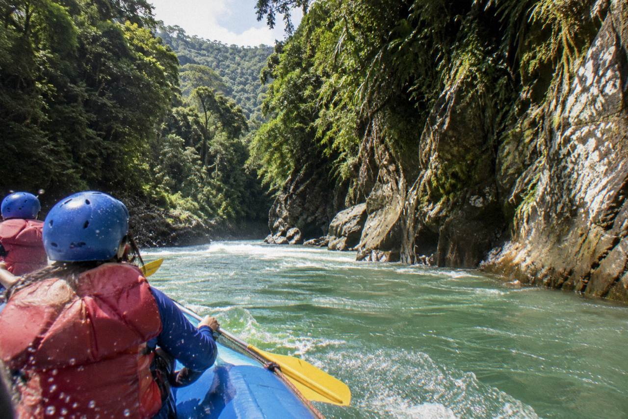 Raft cutting through a green rainforest gorge on the Pacuare River with spray over the bow