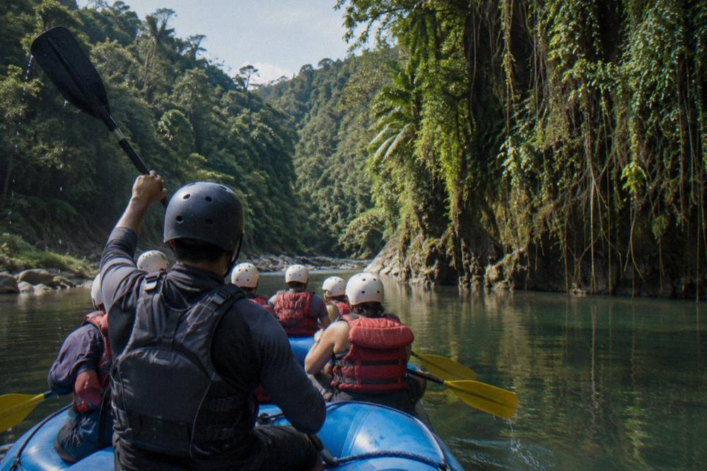 Rafting guide giving paddle commands to a crew in helmets and life jackets on a jungle river